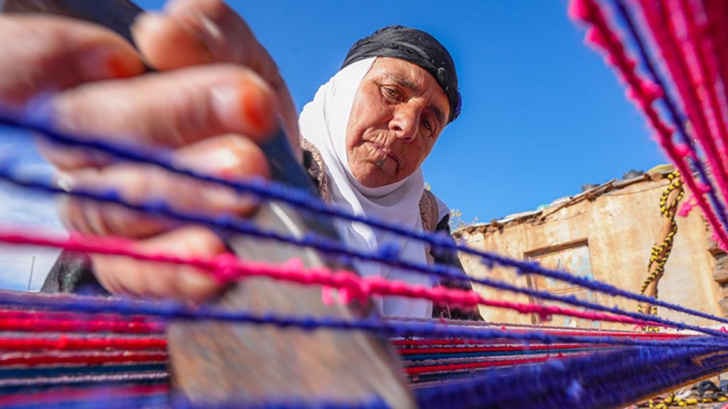 Evinin bahçesindeki tezgahta asırlık yöntemle kilim dokuyor